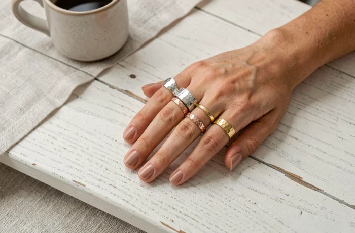 Mains féminines ornées de bagues empilées en or et argent mixtes, tendance bijoux maximaliste 2024 sur table en bois