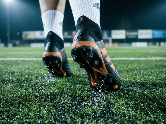Gros plan au ras du sol de crampons Adidas en mouvement sur gazon artificiel mouillé lors d'un match hebdomadaire